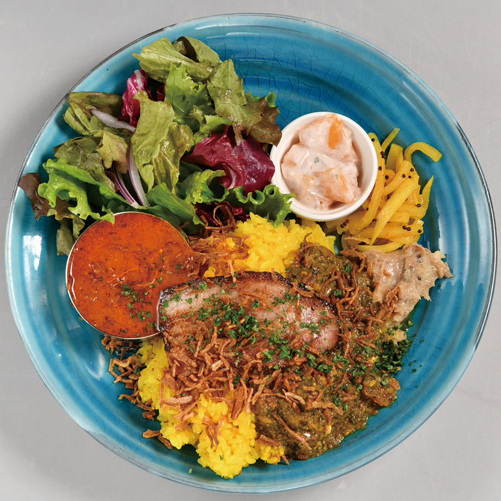 「カリーW」定番のエビカリーと週替わりの2種、インド風の副菜3種、サラダ、日本米のターメリックライス、フライドオニオンがひと皿に。900円。