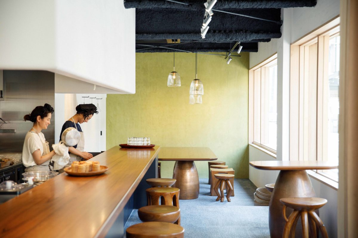 イエローグリーンの壁がカフェの爽やかさを演出している。一脚ずつデザインが異なるスツールはチークを一本彫りしたもので、こちらも〈ババグーリ〉のオリジナルアイテム。