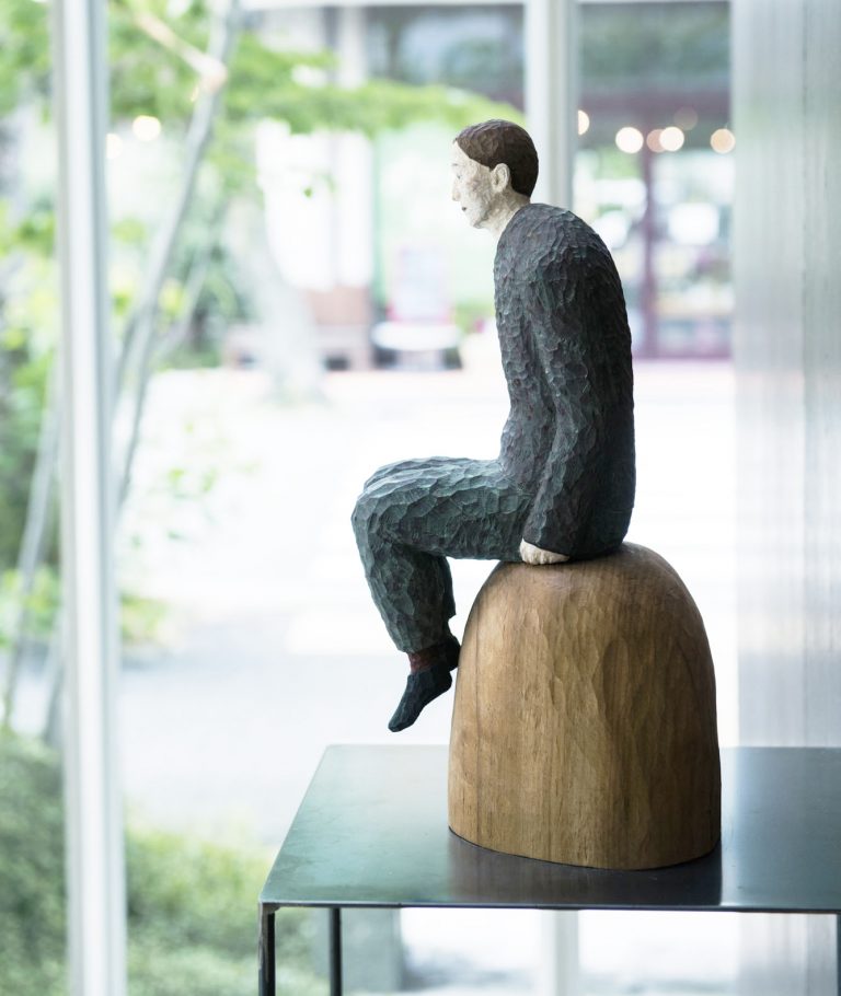 ホテルのエントランスで迎えてくれる穏やかな木彫人物像は、アーティスト丸尾康弘の作品。 高知 〈7days Hotel Plus〉