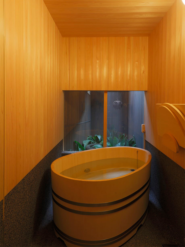 中村の建築の特徴である曲線美がヒノキの風呂にも。浴室の足元に切り取られた窓から自然光が差し込み気持ちがいい。
