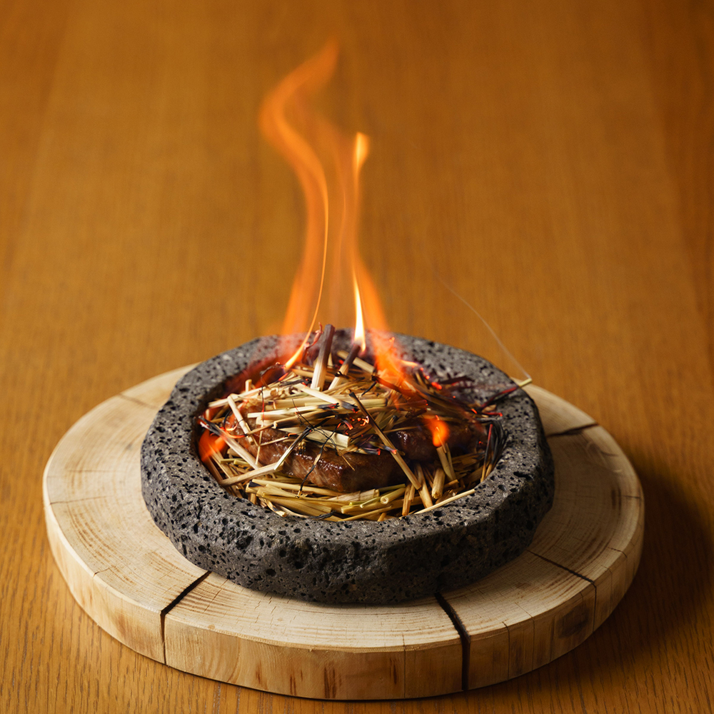 溶岩石と藁を使ったメイン料理「山梨牛黒胡椒焼き」はテーブルで炎をあげて仕上げる演出。