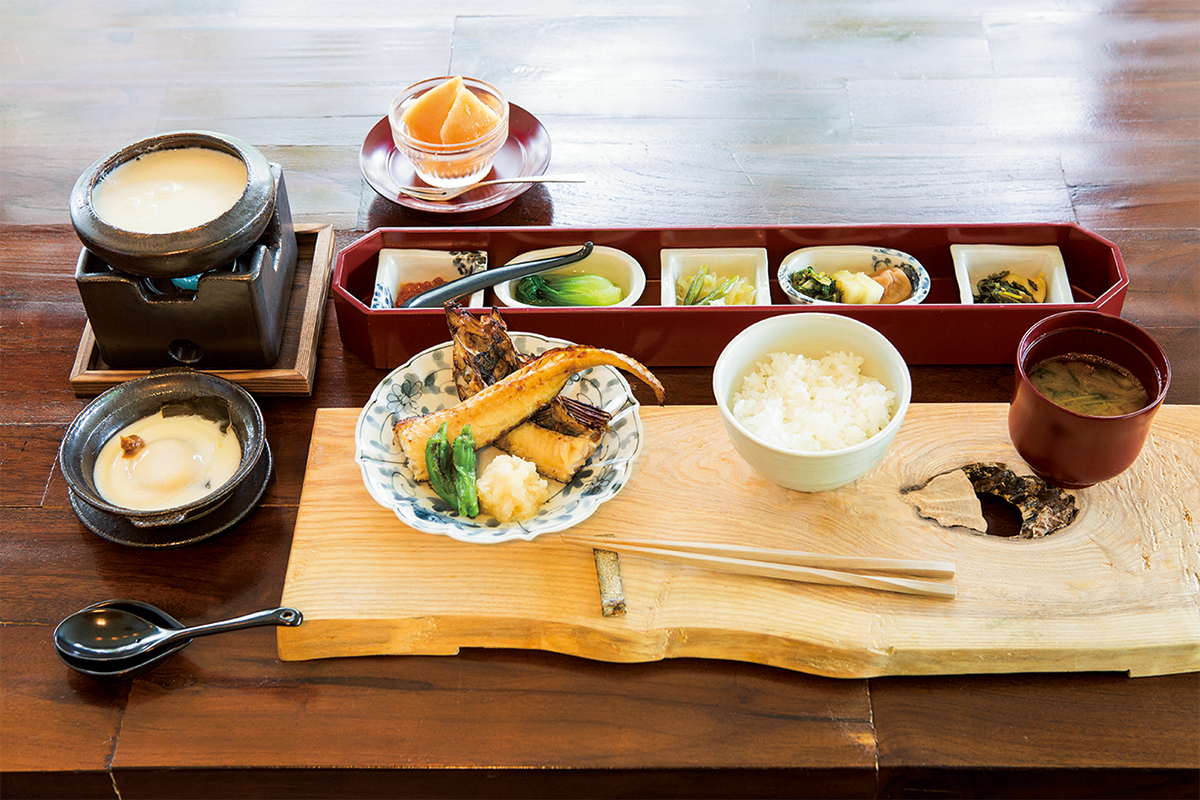 朝食は野菜の小皿、牛乳豆腐、焼き魚。日本一といわれる地元のお米を羊蹄山の湧き水で炊き上げる。新緑を眺めながら。