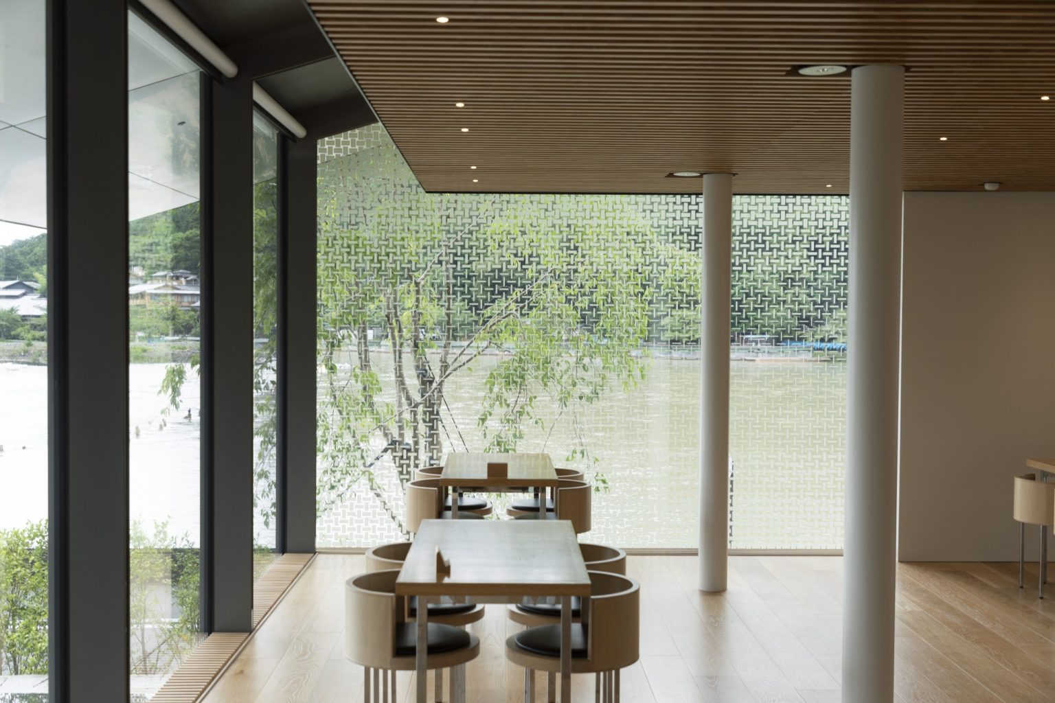 緑と水を感じながらくつろげるカフェスペース。深いひさしがガラスの反射を抑え、外の景色を美しく映し出す。家具と床には無垢材を使用。