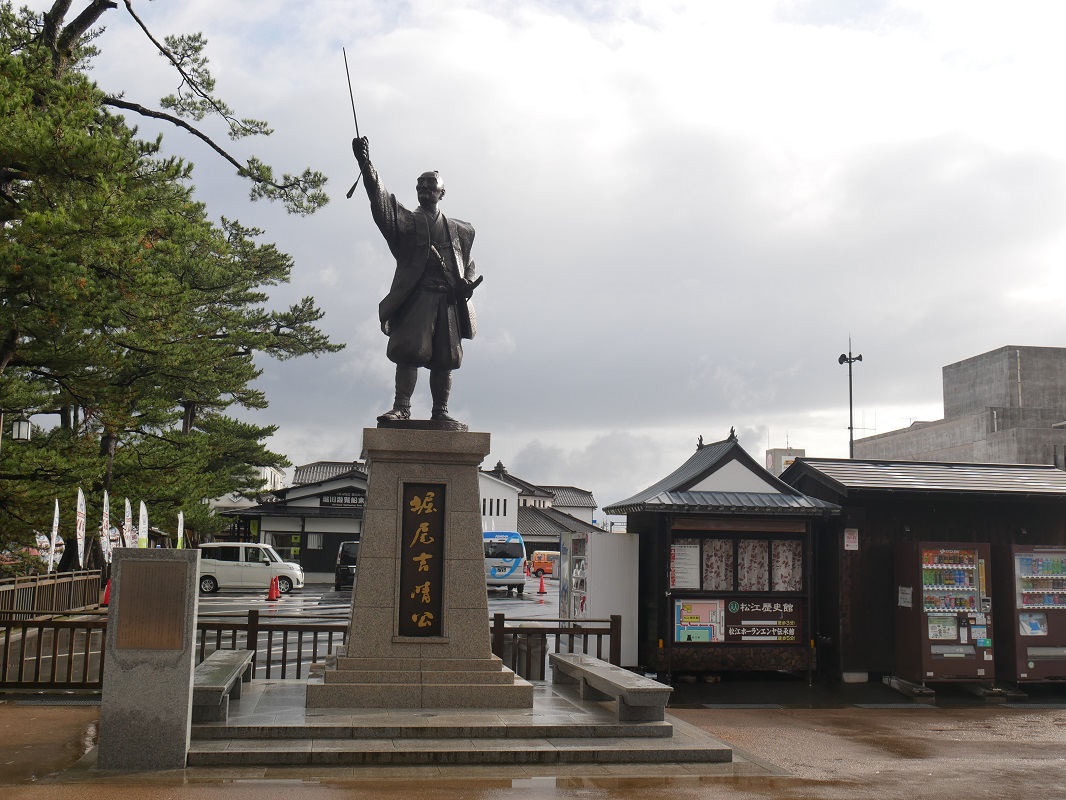 〈松江城〉と城下町を築いた松江開府の祖・堀尾吉晴の像。　