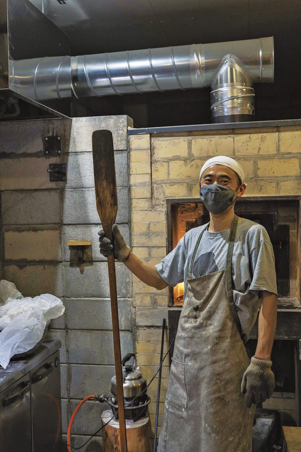 店主の塩見聡史さん。修業先である沖縄の薪窯パン屋〈宗像堂〉で卒業記念にもらったピールを手に。