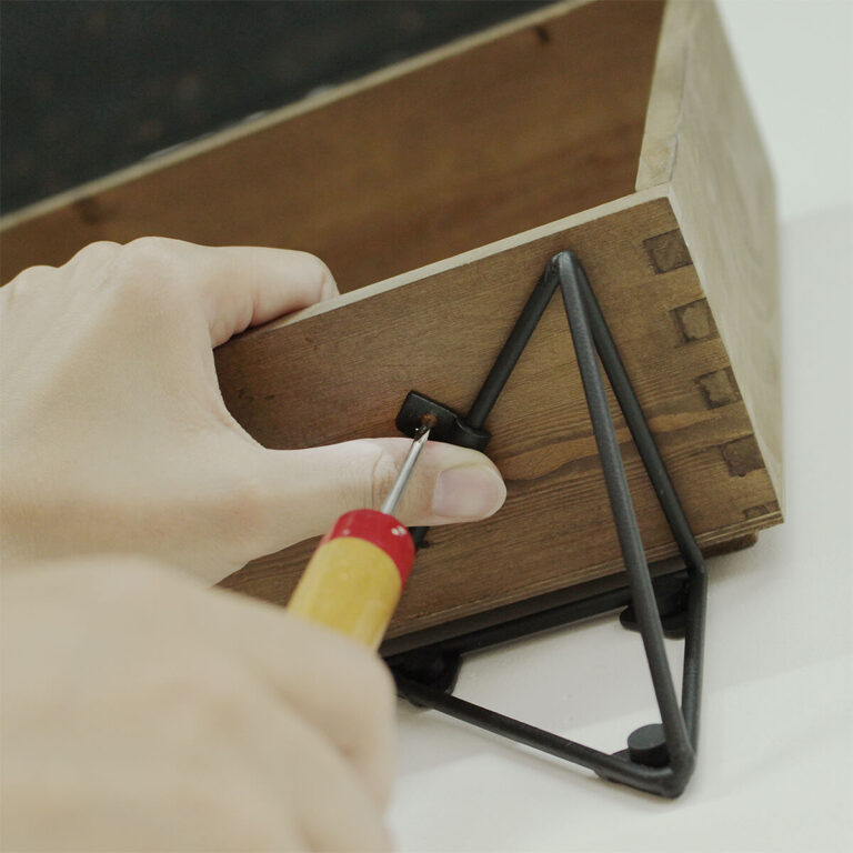 工程2：上に乗せる木箱を置き、固定用のパーツをセットしたら、ネジを留める部分から木箱に向かってキリで下穴をあけます。