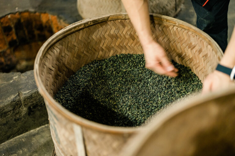 竹カゴに入れられた茶葉はゆっくりと炭火で燻される。均一に火が回るように手で混ぜる。