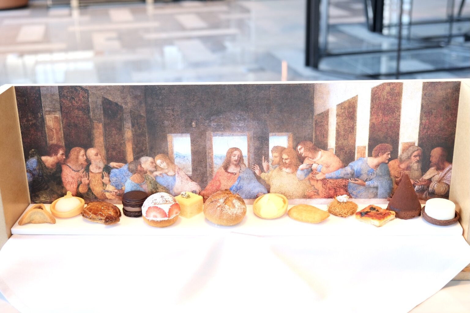 左から順にハマンの耳（バルトロマイ）、レモンのシャーベット（小ヤコブ）、魚の形のミートパイ（アンデレ）、チョコサンド（ユダ）、マリトッツォ（ペテロ）、レバニ（ヨハネ）、パン・ド・カンパーニュ（イエス）、クルフィ（トマス）、タルタ・デ・サンティアゴ（大ヤコブ）、キュネフェ（フィリポ）、ピッザ・マルゲリータ（マタイ）、ティラミス（タダイ）、マハラベイヤ（シモン）。