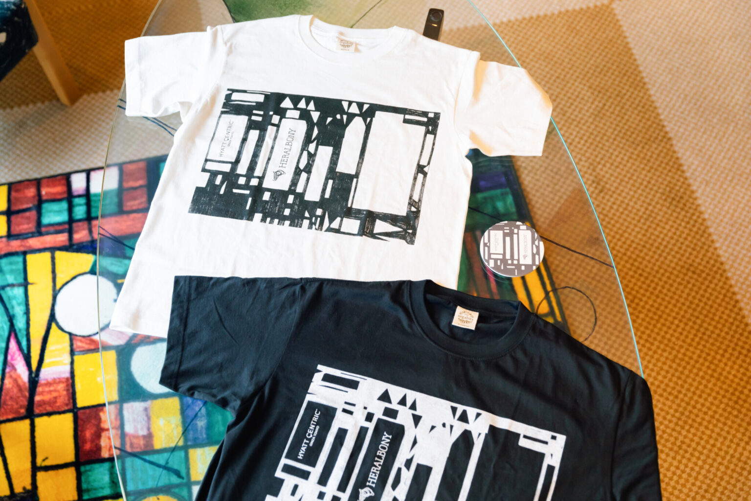 〈るんびにい美術館〉の八重樫季良さんの作品「（無題）（家）」が描かれたオリジナルTシャツとコースター。
