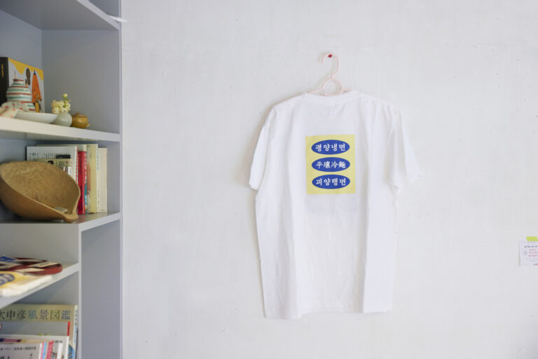 5. 韓国アーティストのTシャツ。平壌冷麺のプリントの T シャツを販売。韓国のアーティストmionjeonさん作。Tシャツは3,000円、バッジもあり。山口さんが直輸入している。