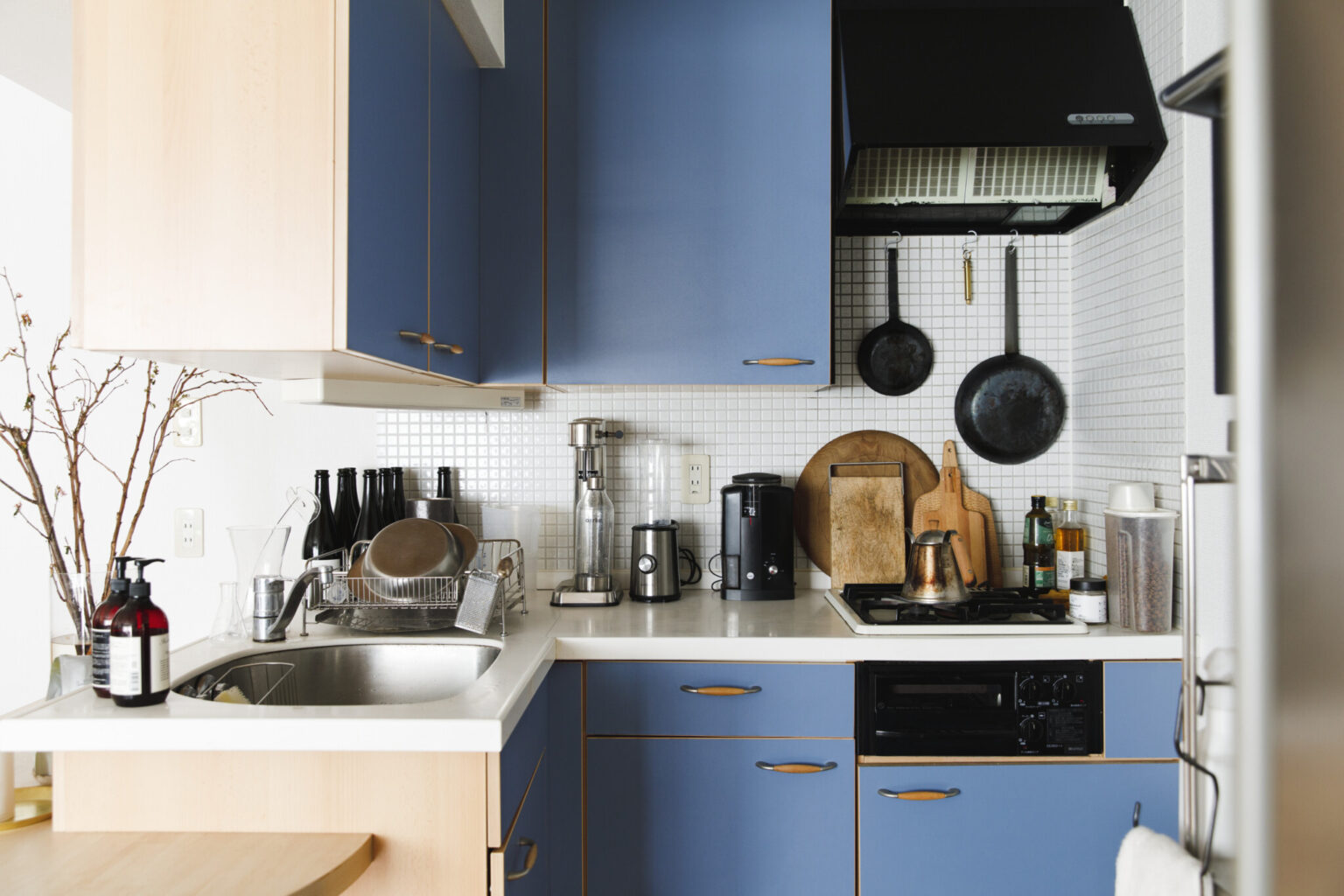クラシカルなブルーのL型キッチンでは、テレビを観ながら料理をするのがお決まり。キッチンアイテムはウッド系やステンレスなど、長く使えるデザインで統一。必要最低限のものをすっきり収納している。