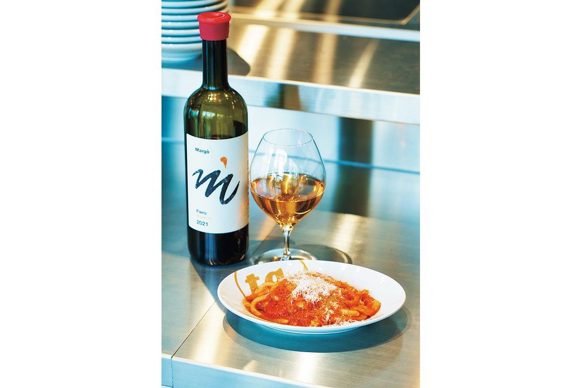 カウンターは、立ち飲みスペースとしても利用できる。イタリア・トスカーナ州の郷土料理「ピチ・アリオーネ」1,100円は、ニンニクとチーズの効いたトマトソースで。オレンジワインはグラス800円〜。