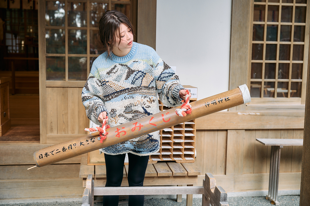 女性の願いをひとつだけ叶える「神明神社」の巨大おみくじを引く様子。