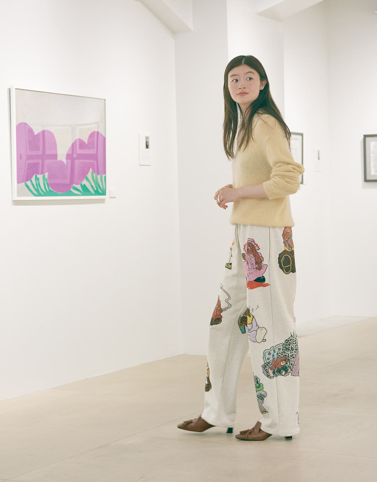 ギャラリーに訪れるときは、パンチを利かせた装いに。上質な素材のシンプルなニットに、目を惹く犬のイラストがプリントされたスウェットパンツを合わせて遊び心たっぷりに。スキッパーポロニット51,000円（エイトン｜エイトン青山 03-6427-6335）／スウェットパンツ48,400円（シーロン info@siiilon.com）／スパイラルトリプルリング 3,850円（ロニ loni_info@auntierosa.com）／タッセルパンプス34,100円（ヨシト｜ニューロンドン 03-5603-6933）