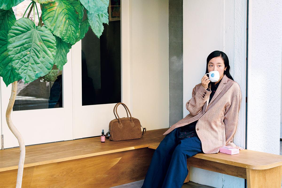 ゆったりと川を眺めながらコーヒーが飲めるテラスベンチで気分よく。ジャケット60,500円、パンツ27,500円（共にアップサイクルリノ）、バッグ27,500円
（オウレンティ｜全てネストローブ 表参道店 03-6438-0717）／中に着たシャツ27,500円（ヤエカ カンバス デザイン｜ヤエカ 03-6426-7107）
